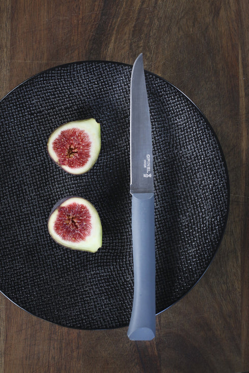 Couteau Bon Appétit+ anthracite sur une assiette noire avec des figues